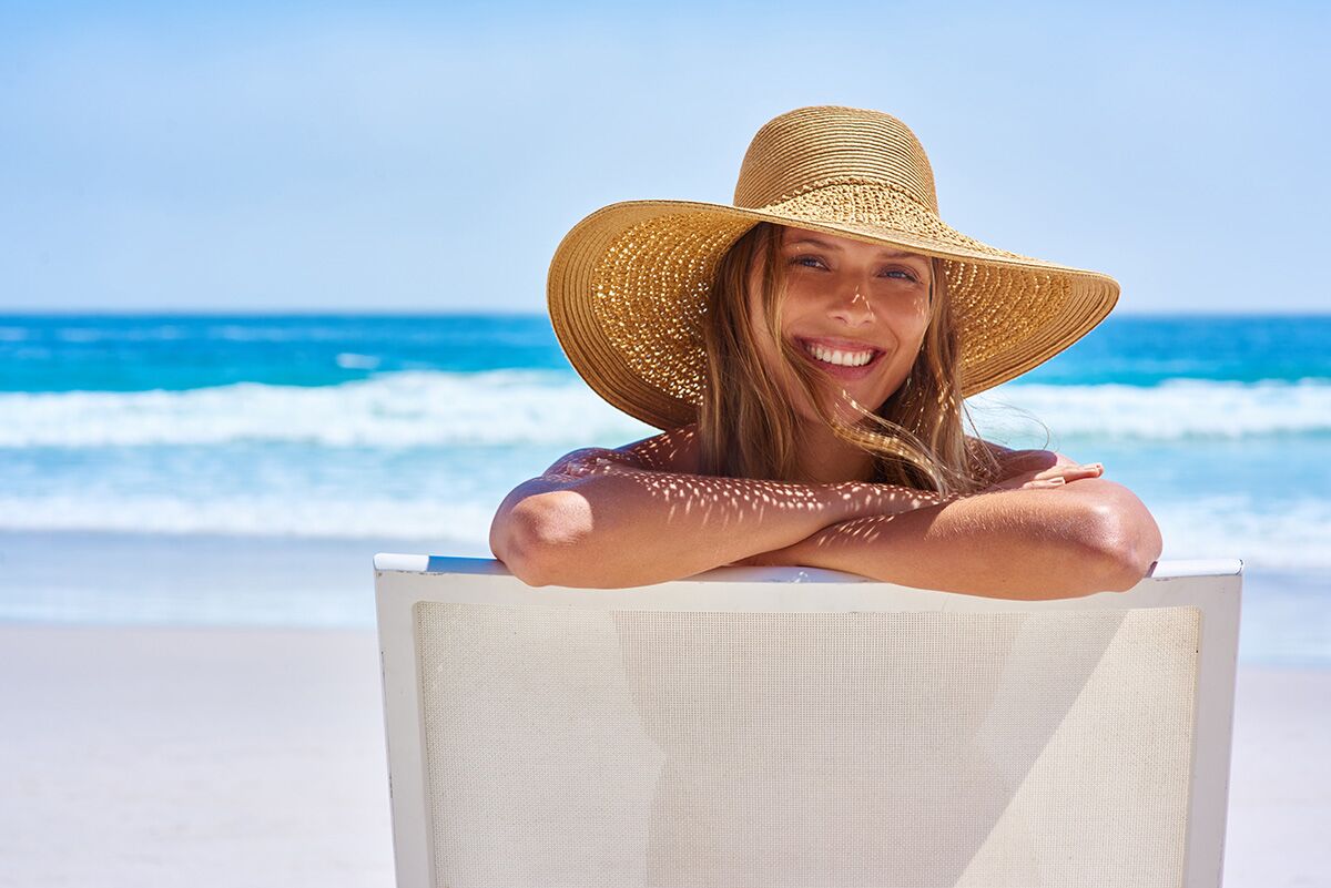 Girl on beach with floppy hat. Blue sea behind