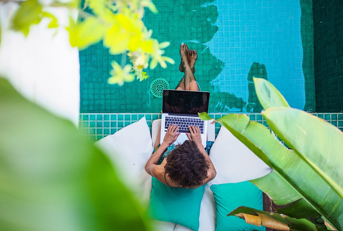 Girl working on laptop dipping feet in the swimming pool.